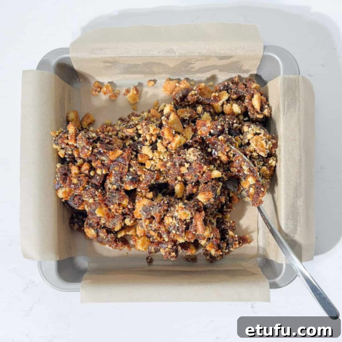 Effortless Date Bars 16 Scooping the sticky date and biscuit mixture into the parchment-lined square baking pan.