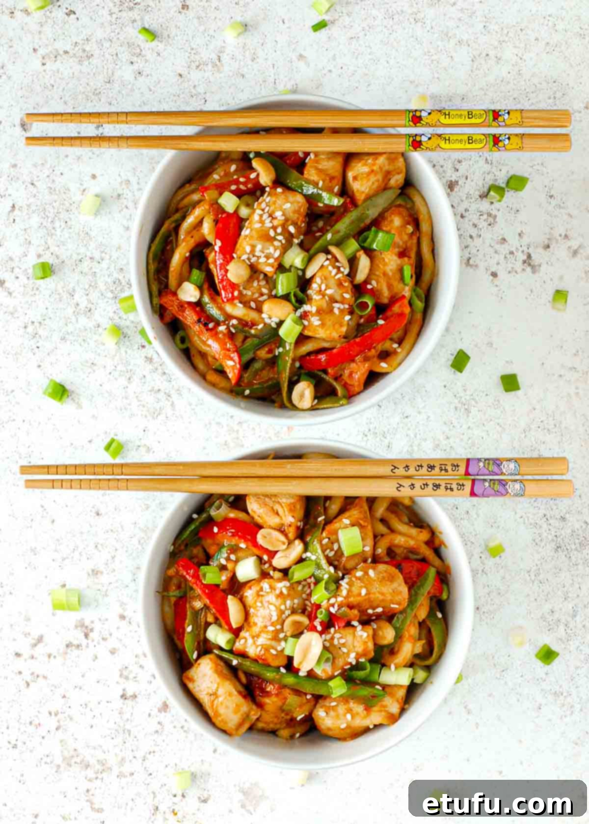 Two bowls of creamy Satay Chicken Stir Fry with Udon noodles on a pristine white background, beautifully garnished and ready to be enjoyed with chopsticks.