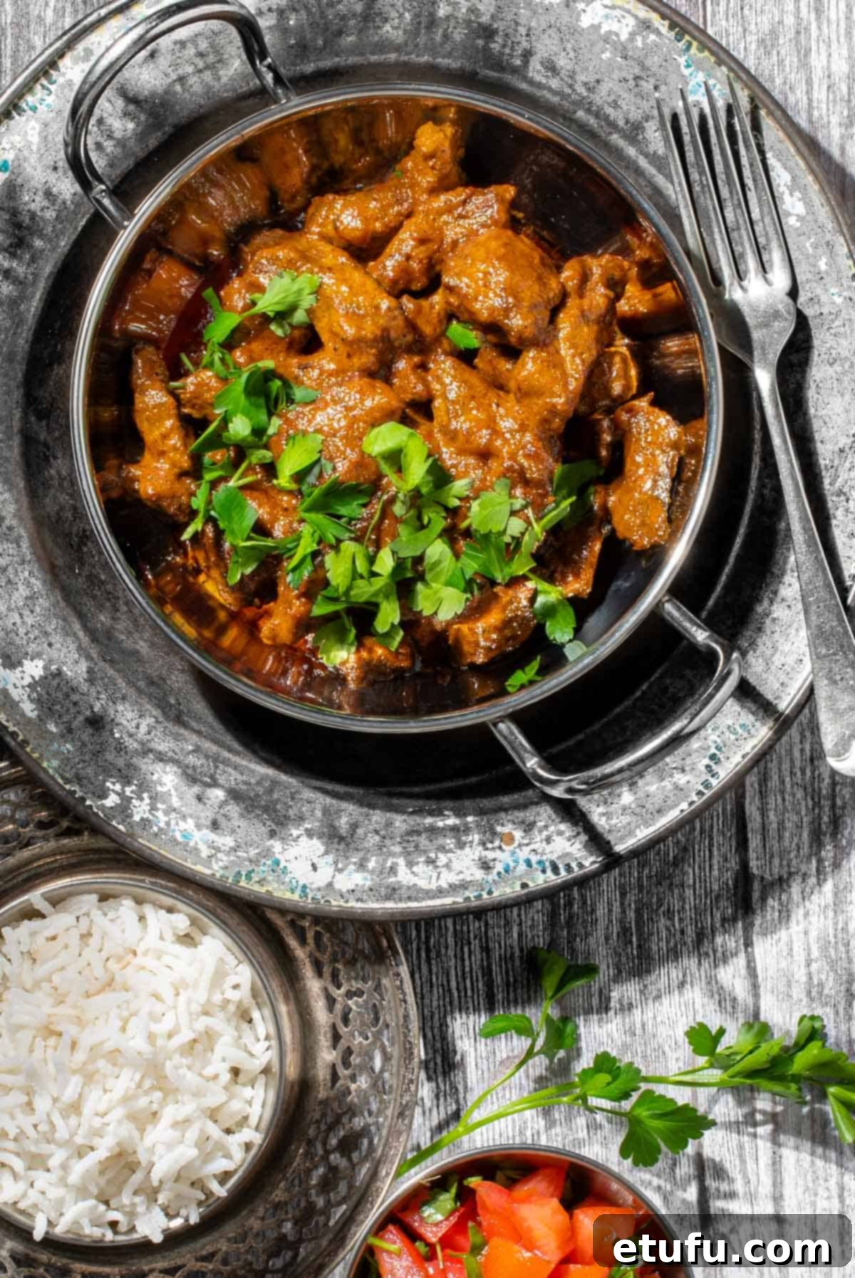 Aromatic beef curry with coconut milk in a balti bowl with a side of rice.
