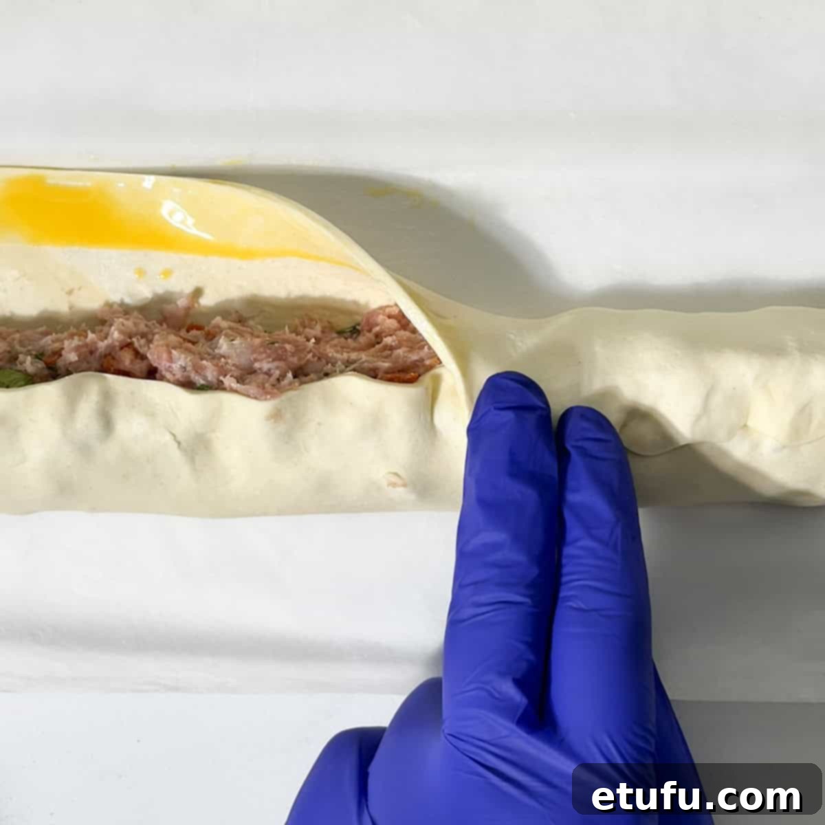 Folding the pastry over the sausage roll filling.