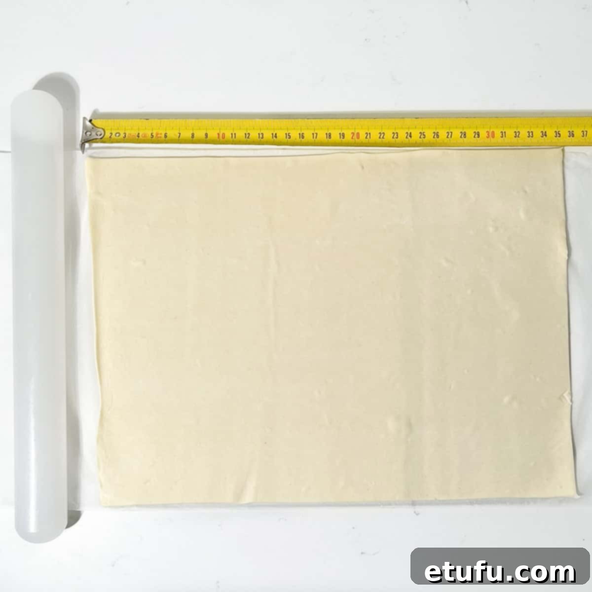 Measuring the puff pastry sheet with a measuring tape.