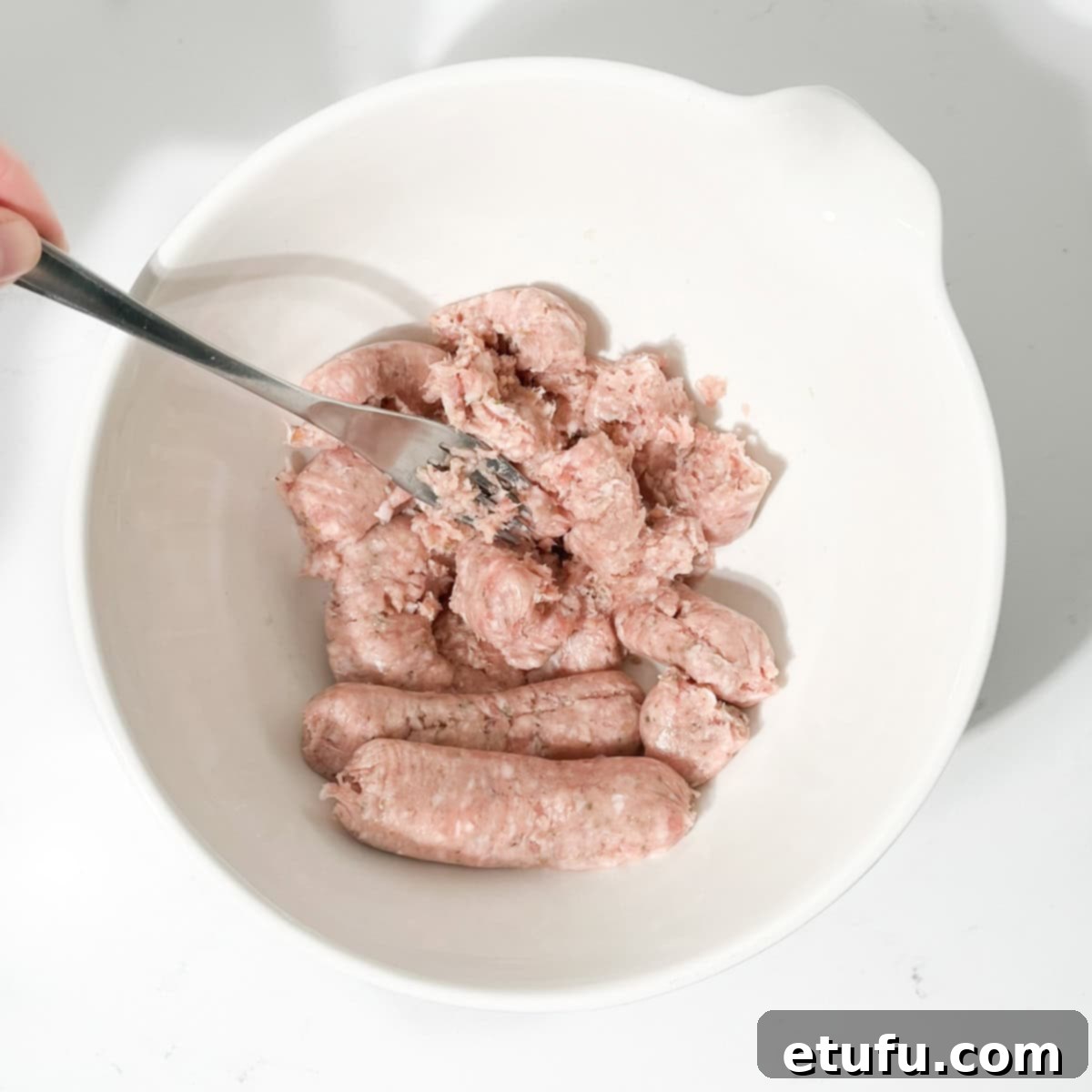 Breaking up the sausage meat in a large white bowl.