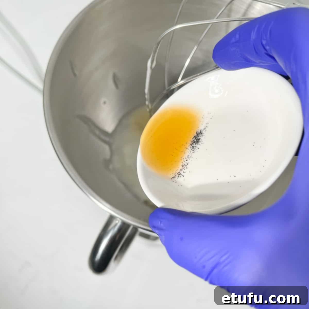 Vanilla extract being added to the warm egg and sugar mixture in the stand mixer bowl.