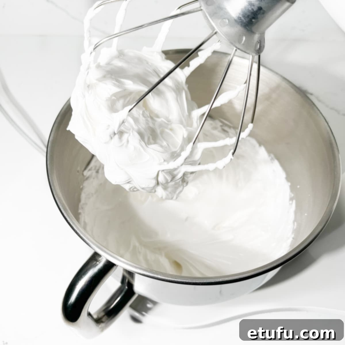 Marshmallow fluff whipped to stiff peaks in the bowl of a stand mixer, showcasing its pure white and glossy texture.