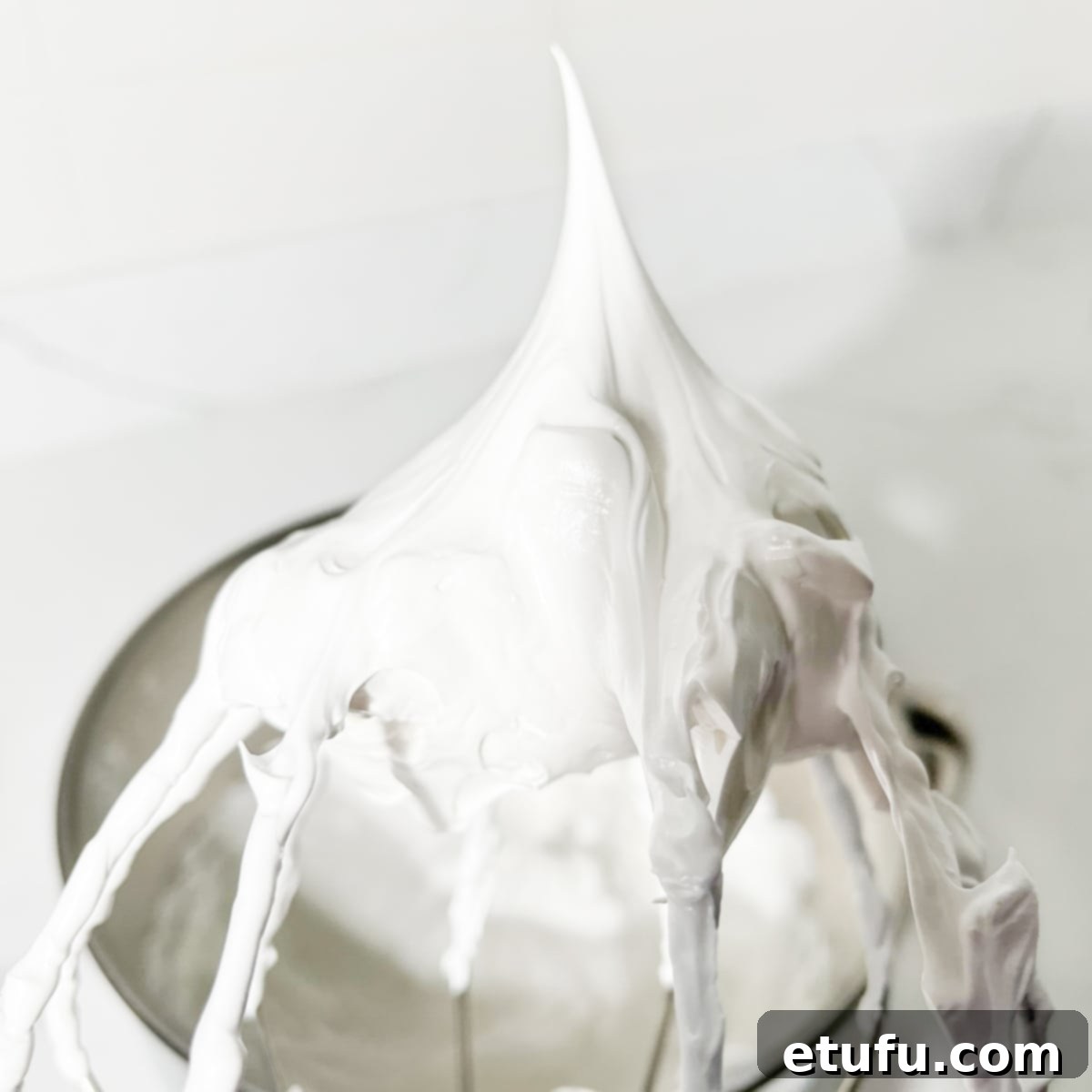 Marshmallow fluff on a whisk showing perfectly stiff peaks, indicating it is ready for use.