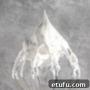 Marshmallow fluff on a whisk with stiff peaks, illustrating the perfect consistency for this homemade treat.