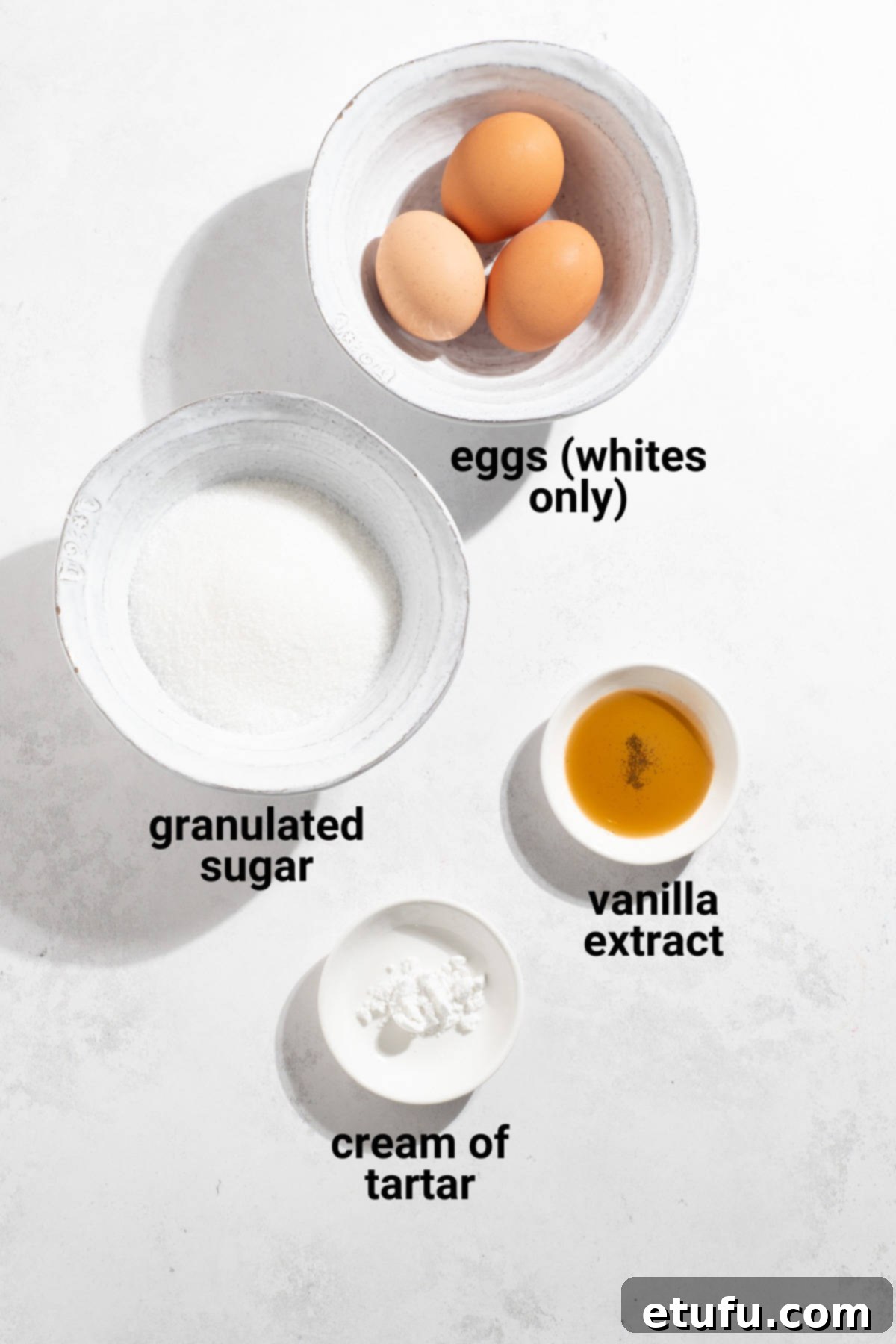 Key ingredients for marshmallow fluff laid out on a table: eggs, sugar, cream of tartar, and vanilla extract.