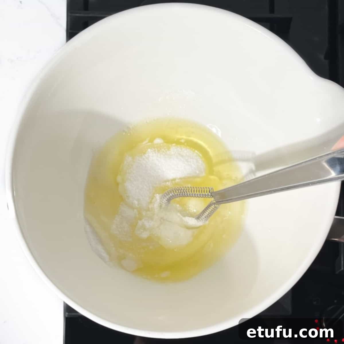 A bowl containing egg whites, sugar, and cream of tartar placed over a saucepan with boiling water on the stovetop.