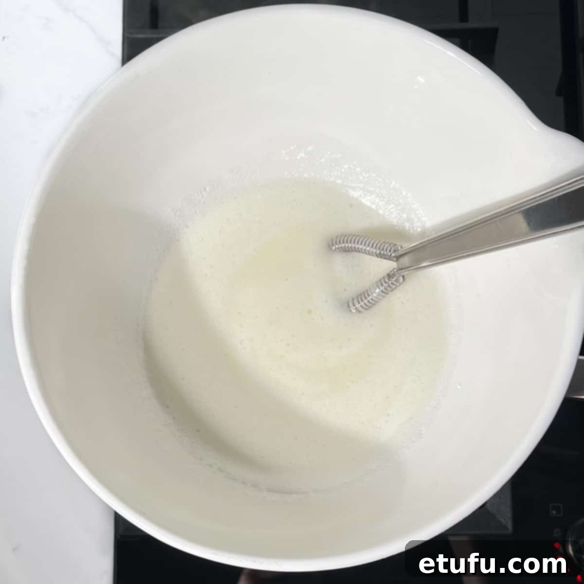 The marshmallow fluff mixture beginning to foam and lighten over the double boiler, indicating the start of the cooking process.