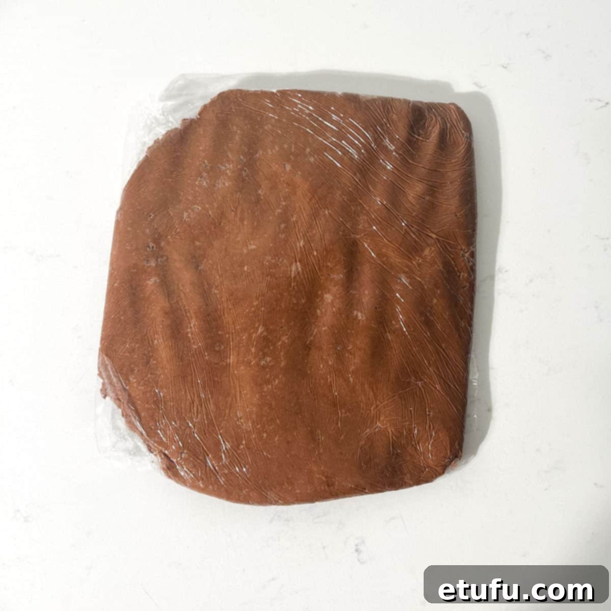 Flattening the chocolate shortbreads dough into a disc, wrapped in plastic wrap.