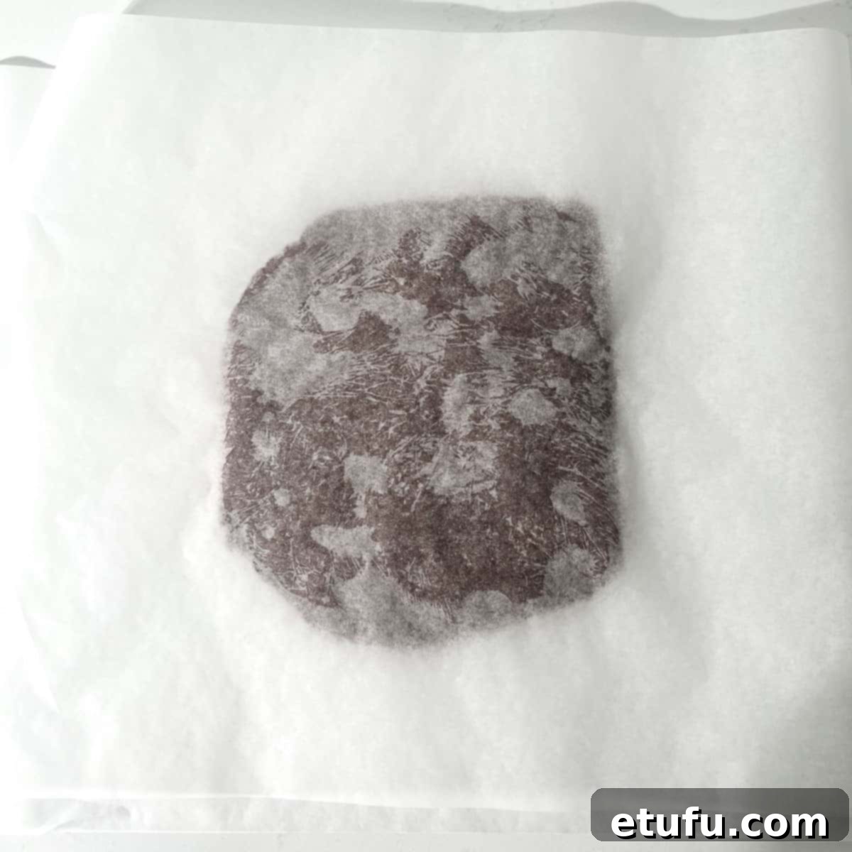 A flat disc of chocolate shortbread dough sandwiched between two pieces of parchment paper.