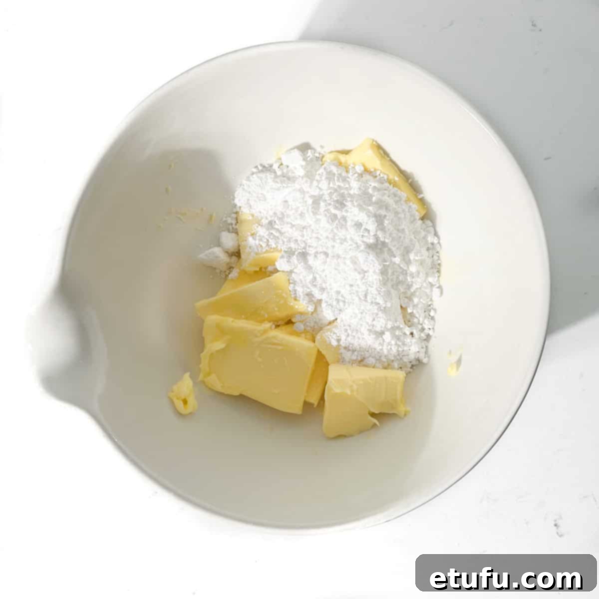 Adding softened butter and icing sugar to a large white bowl.