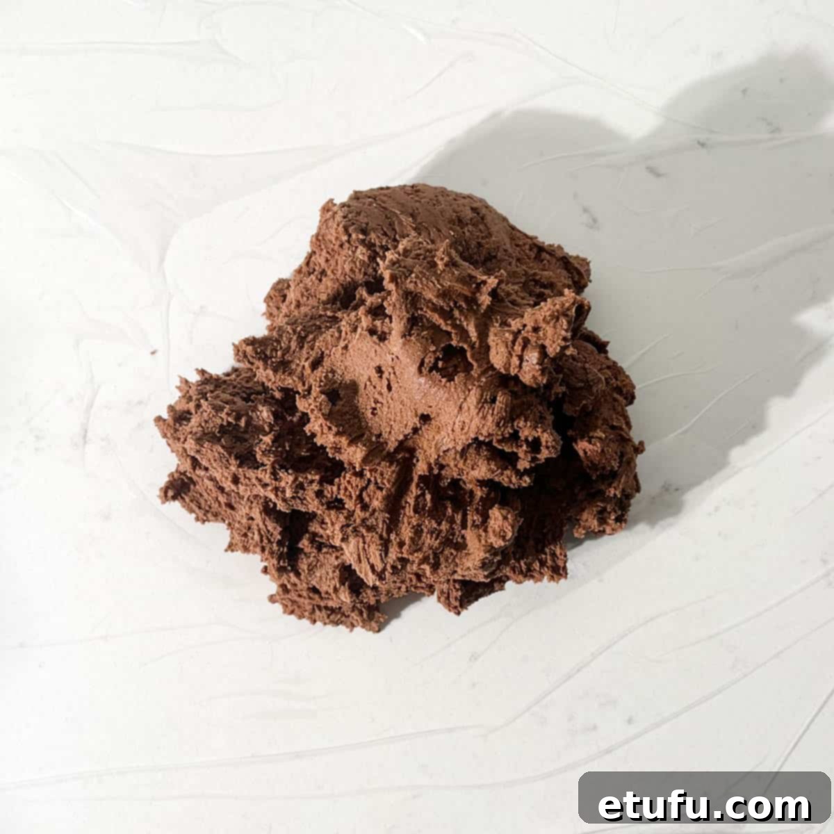 Chocolate shortbread dough tipped out onto a piece of plastic wrap.