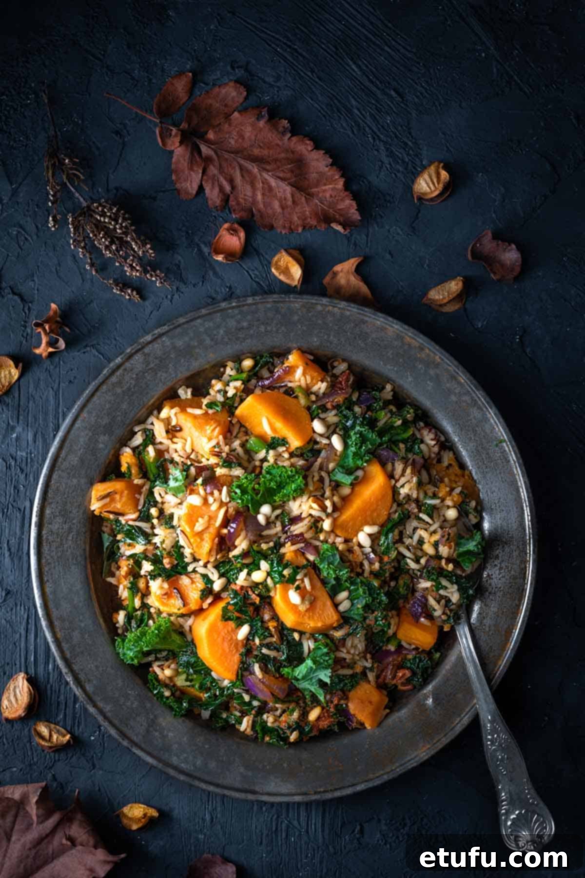 Sweet potato salad in a metal bowl on a dark background, surrounded by autumn leaves