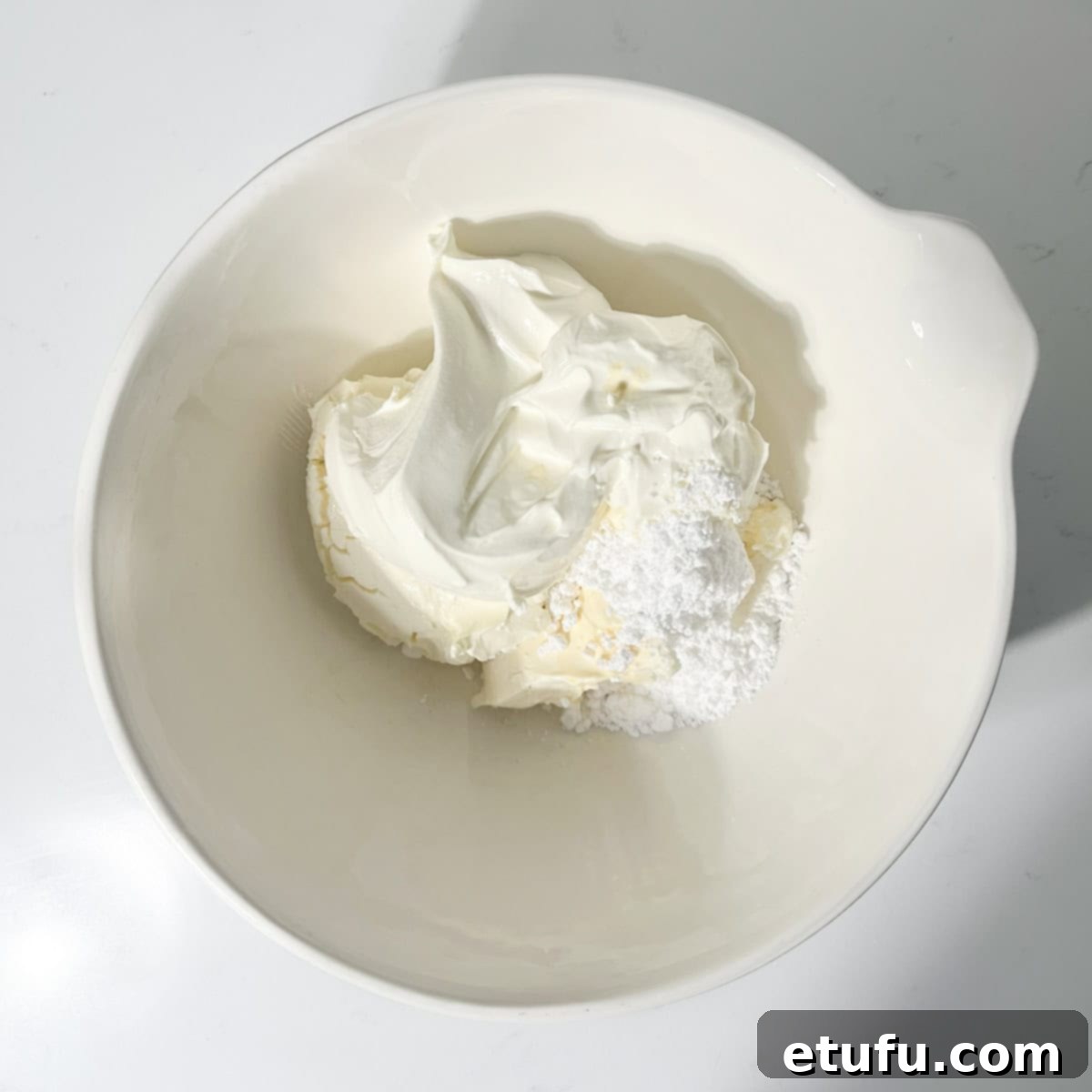 Combining room-temperature cream cheese, mascarpone, icing sugar, and vanilla extract in a large white bowl.