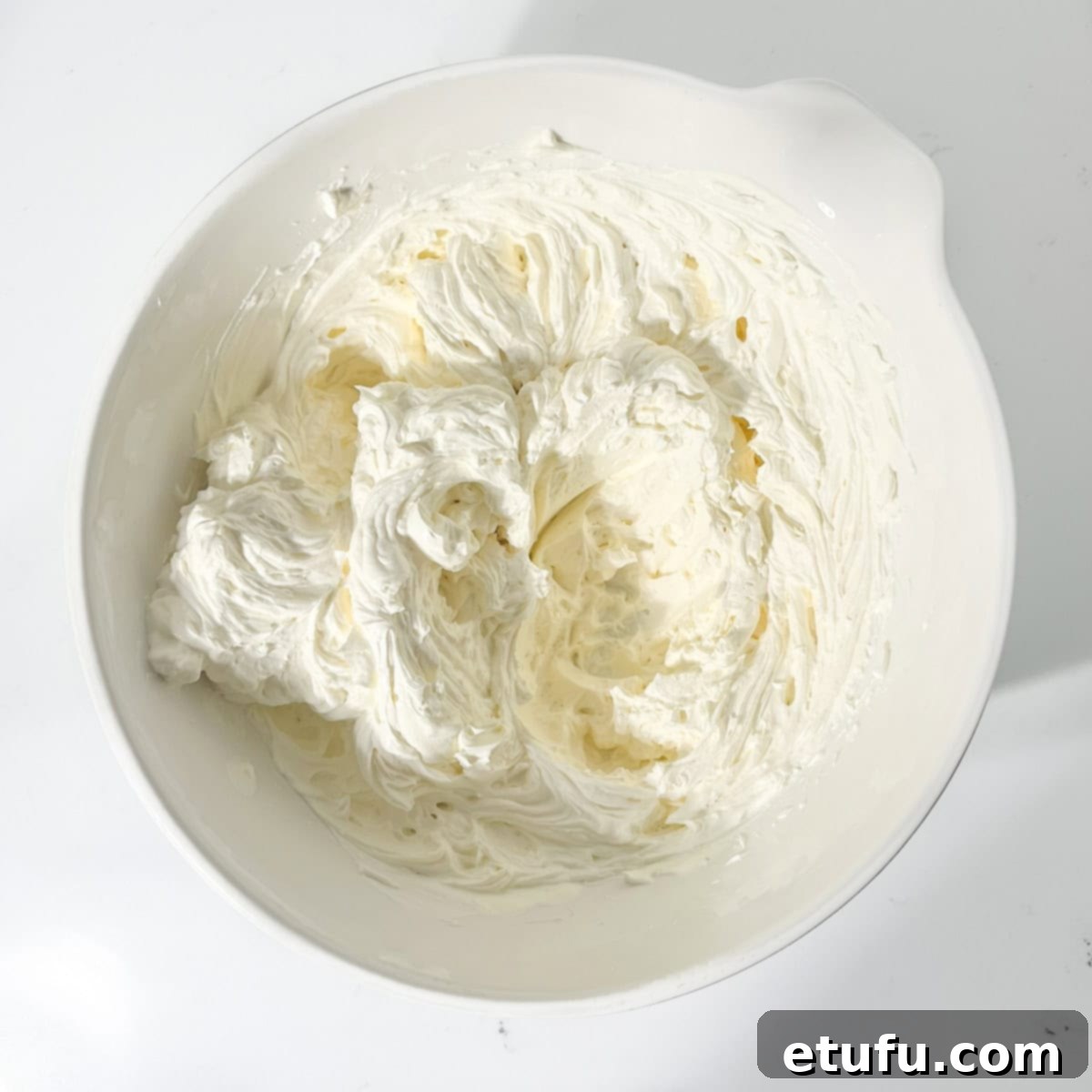 Cream cheese and mascarpone mixture after being whipped to a smooth consistency in a large white bowl.