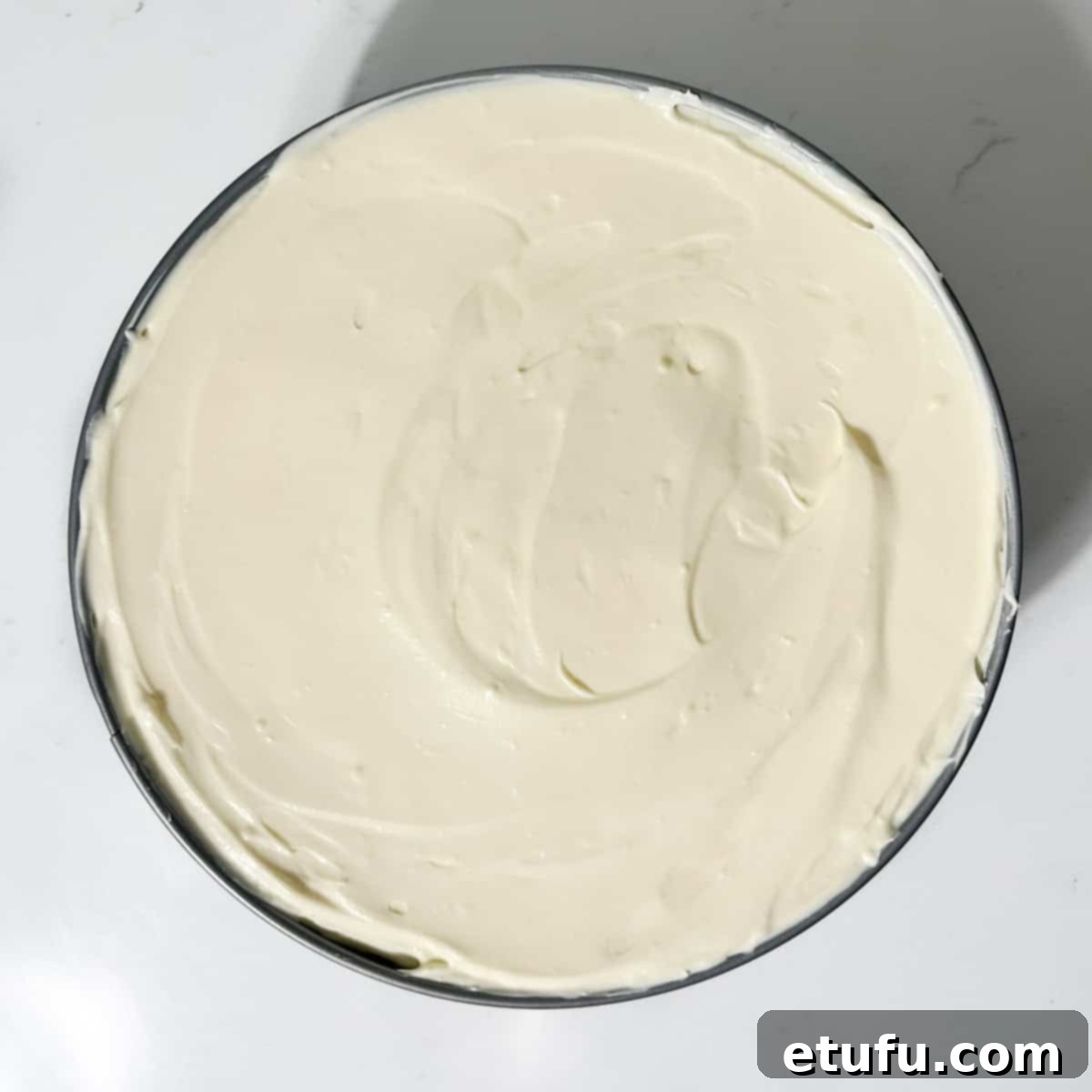 White chocolate cheesecake filling smoothed over the cookie base in a springform tin, ready for chilling.