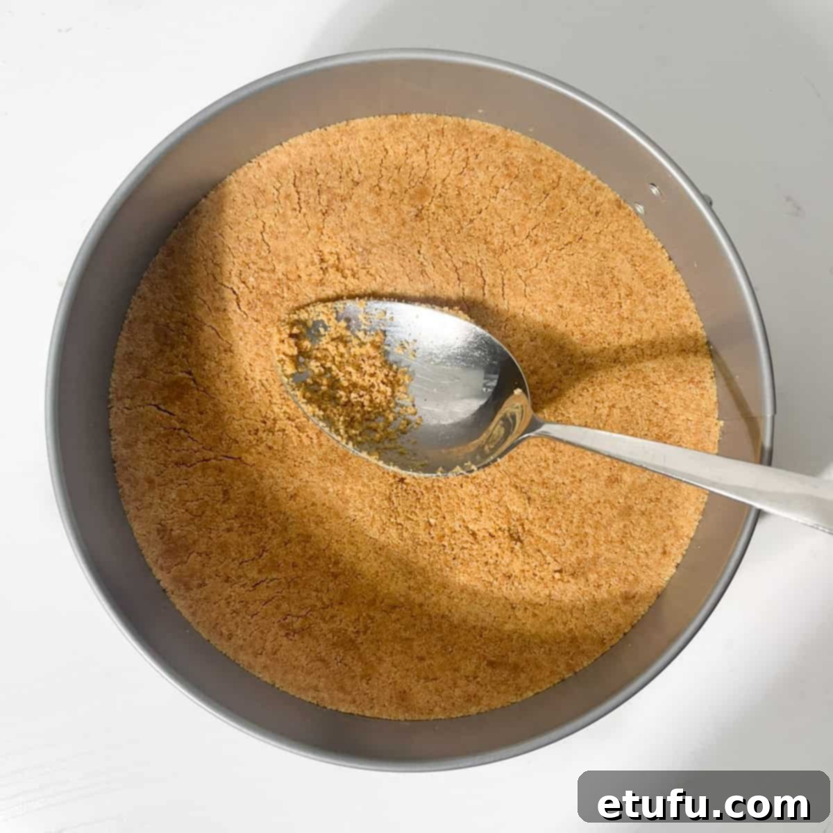 Pressing the cookie crumbs and butter into the base of a springform tin with a large spoon to form the crust.