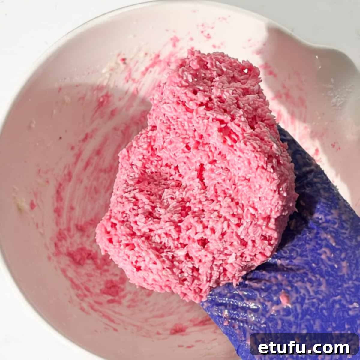 A hand holding the pink half of the coconut ice after it's been mixed.