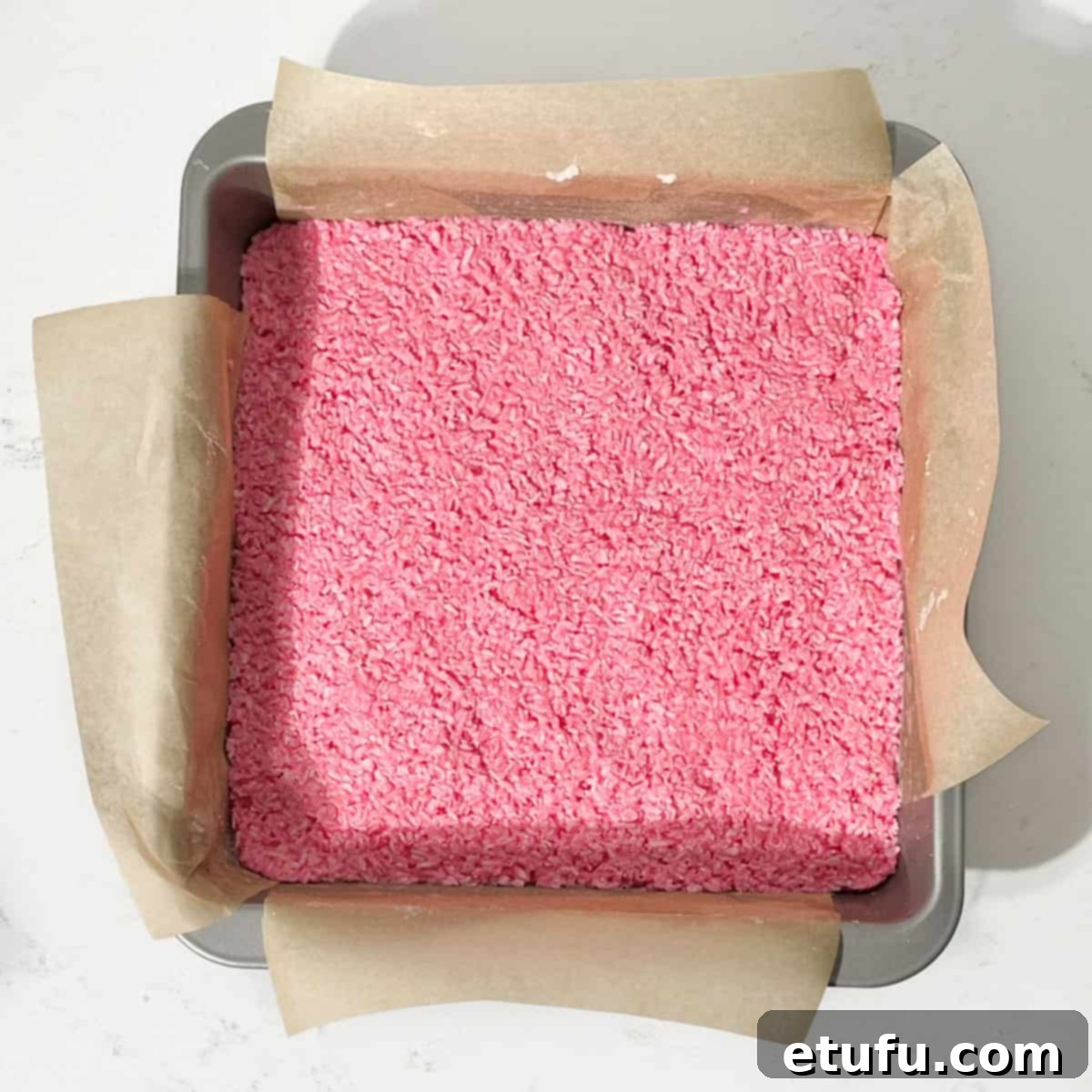 The final layer of pink coconut ice spread into the tin.