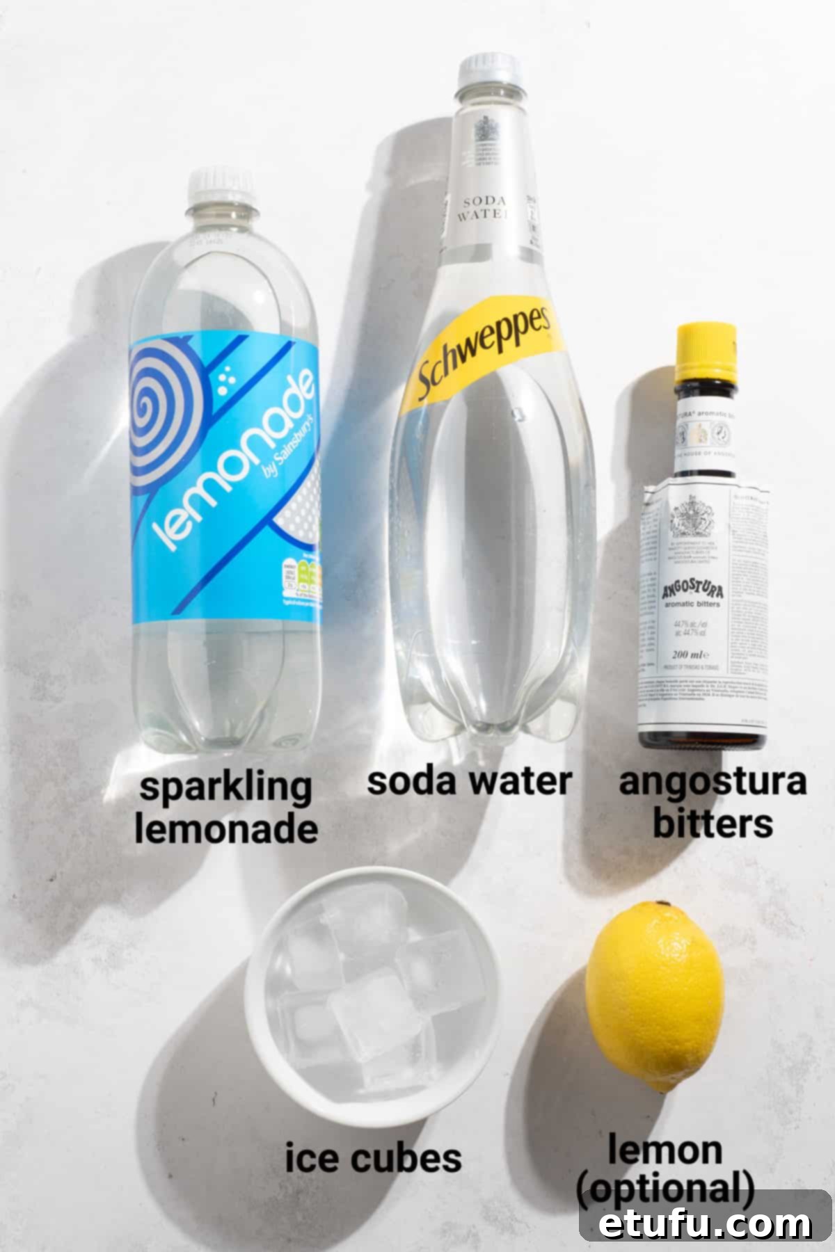 Rock shandy ingredients laid out: lemonade, soda water, Angostura bitters, and fresh lemons.