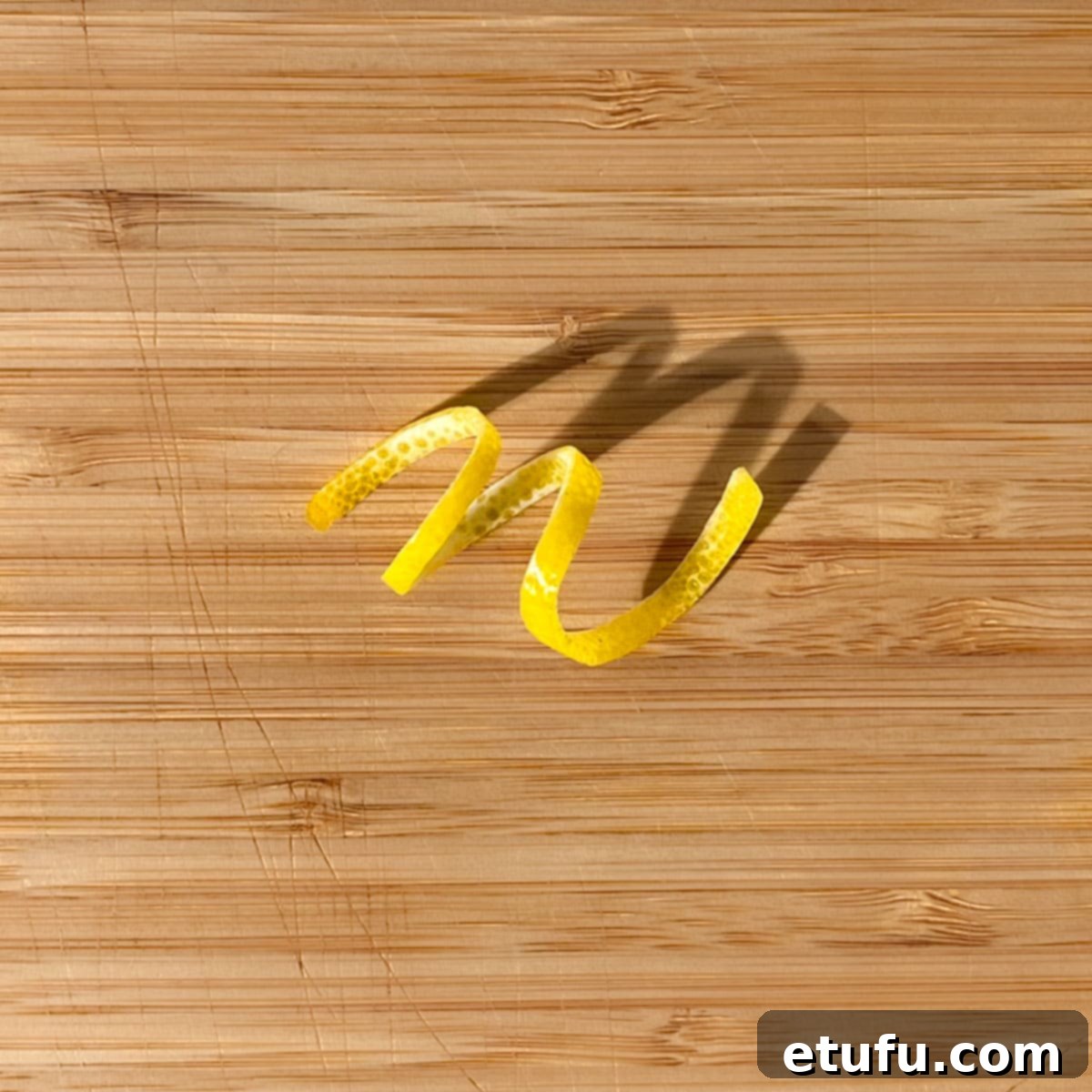 A lemon peel twisty on a wooden chopping board.