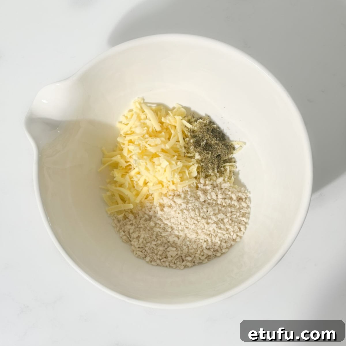 A large white bowl containing a mixture of breadcrumbs, grated cheese, and dried herbs, forming the dry base for the stuffing.