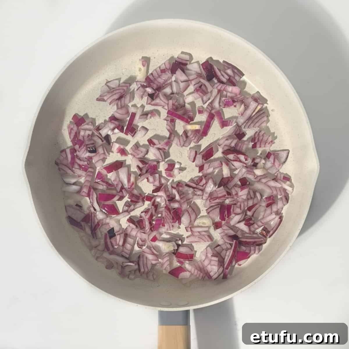 Finely chopped onions sautéing in hot oil in a large frying pan, becoming soft and translucent.
