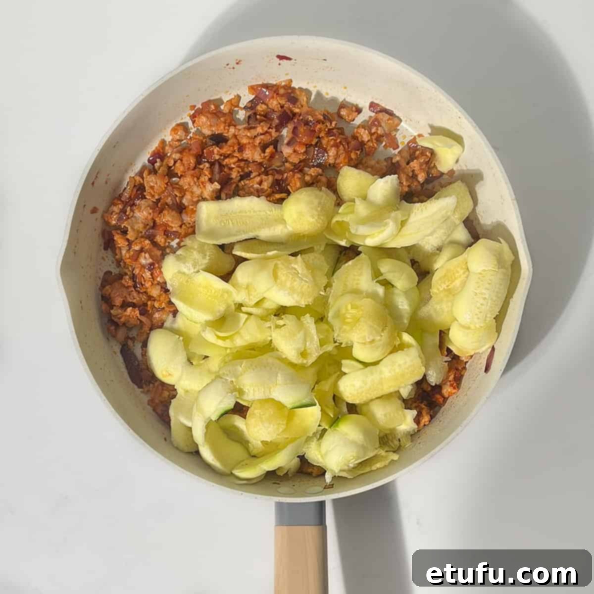 Diced courgette flesh added to the savory sausage and onion mixture in the frying pan, ready to be cooked down.