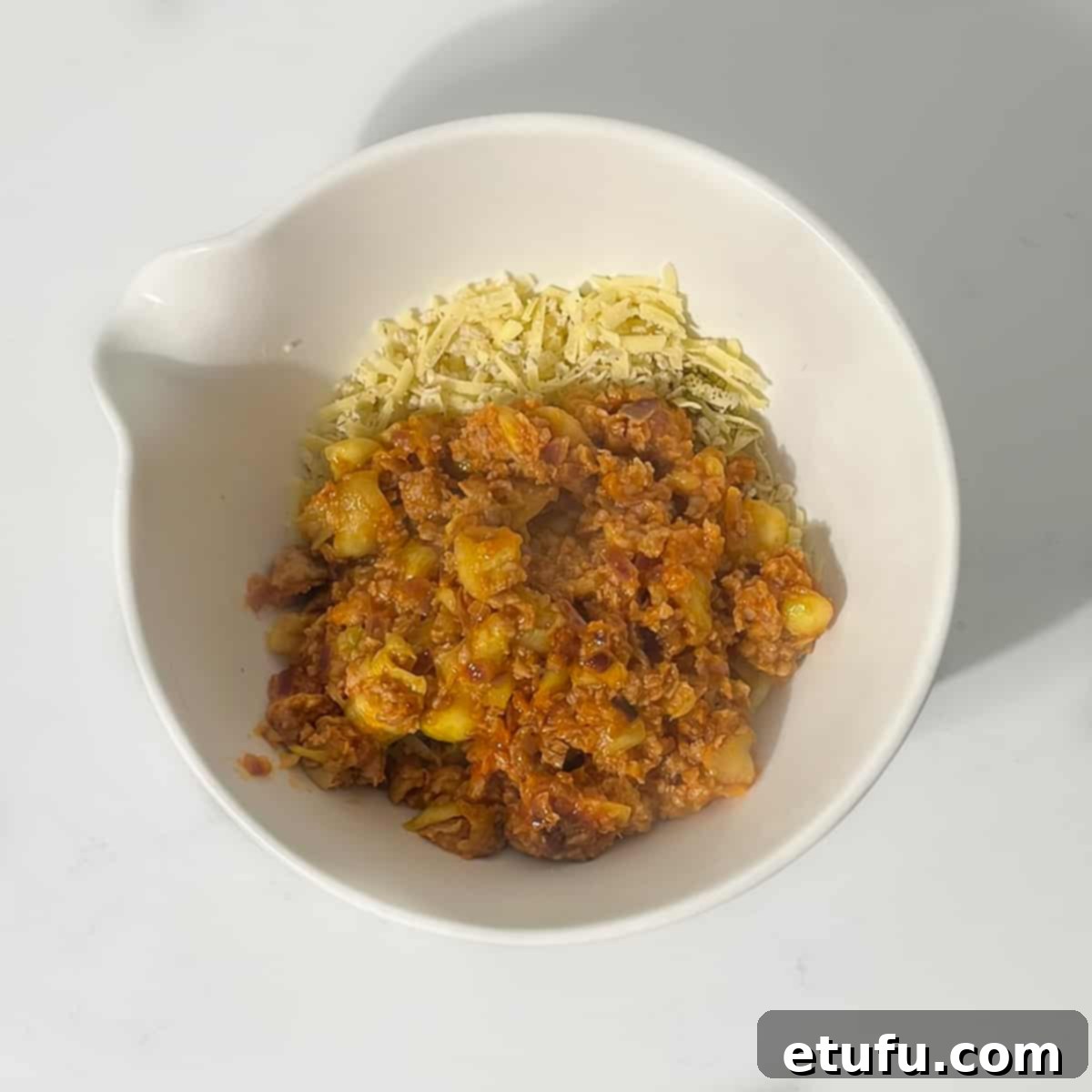 The warm, rich sausage and vegetable mixture being added to the bowl containing breadcrumbs, cheese, and herbs, ready to be combined into the final stuffing.