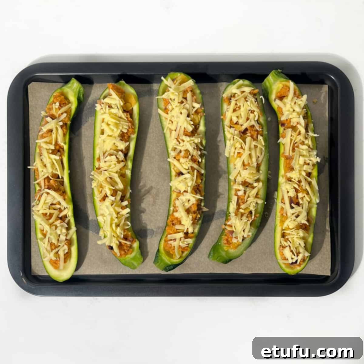 Zucchini boats generously filled with savory sausage stuffing and topped with a layer of grated cheddar cheese, ready for baking.
