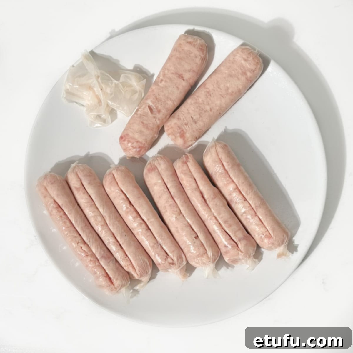 A hand expertly removing the casing from a raw sausage, preparing the meat for the delicious stuffed courgettes recipe.