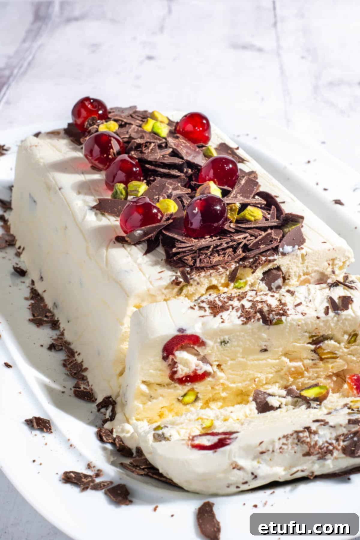 Exquisite Cassata ice cream adorned with glacé cherries, pistachios, and chocolate, elegantly presented on a pristine white serving plate.