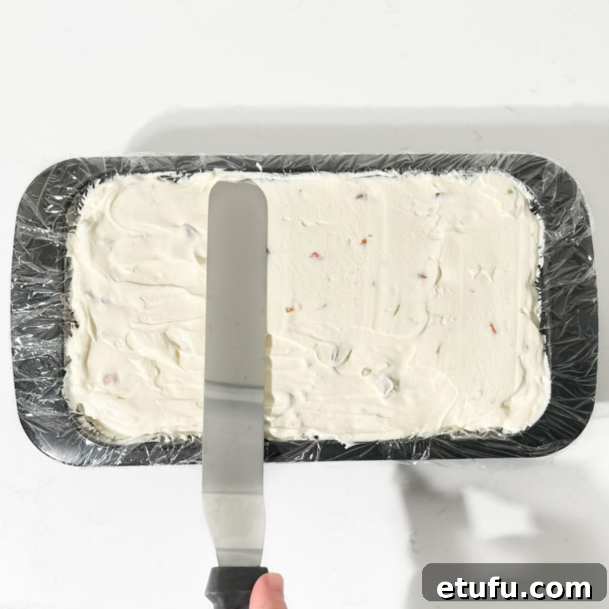 A spatula smoothing the top surface of the Cassata ice cream within the loaf tin, preparing it for freezing to ensure an even bottom when unmolded.