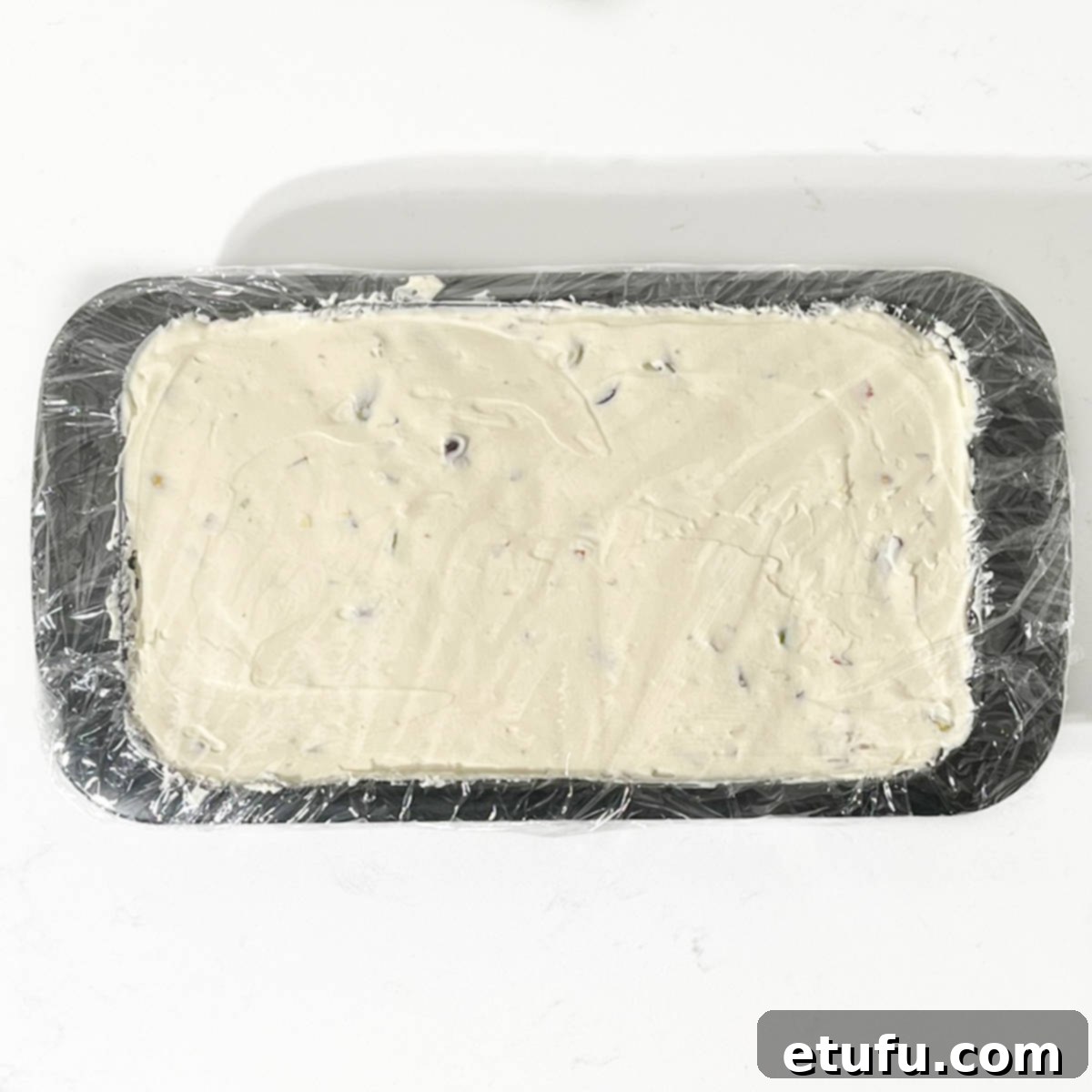 Cassata ice cream in a loaf tin covered with cling film and ready for freezing.