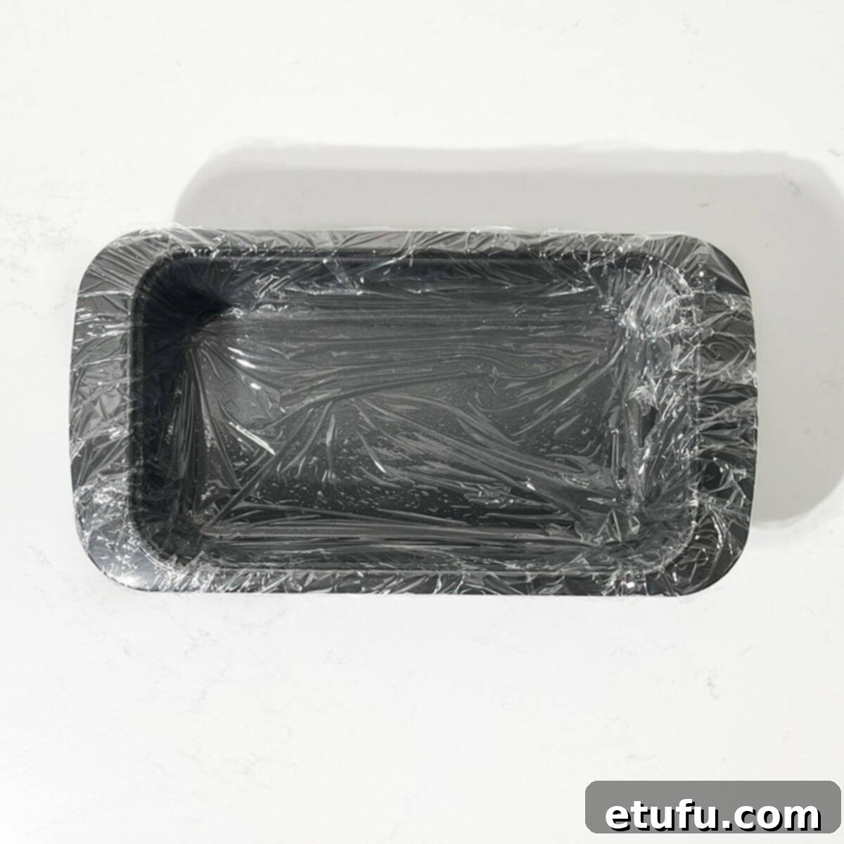 A loaf tin meticulously lined with clear cling film, ready for the Cassata mixture, ensuring easy removal.