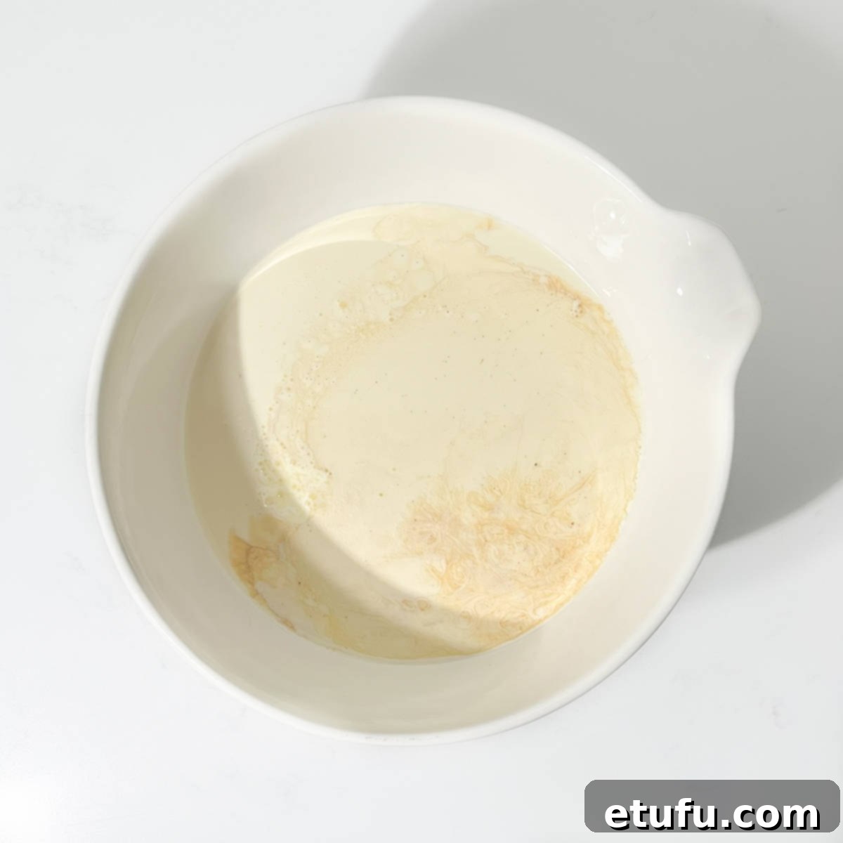 The initial ingredients for no-churn ice cream – heavy cream, condensed milk, and vanilla – being added to a large, pristine white mixing bowl.