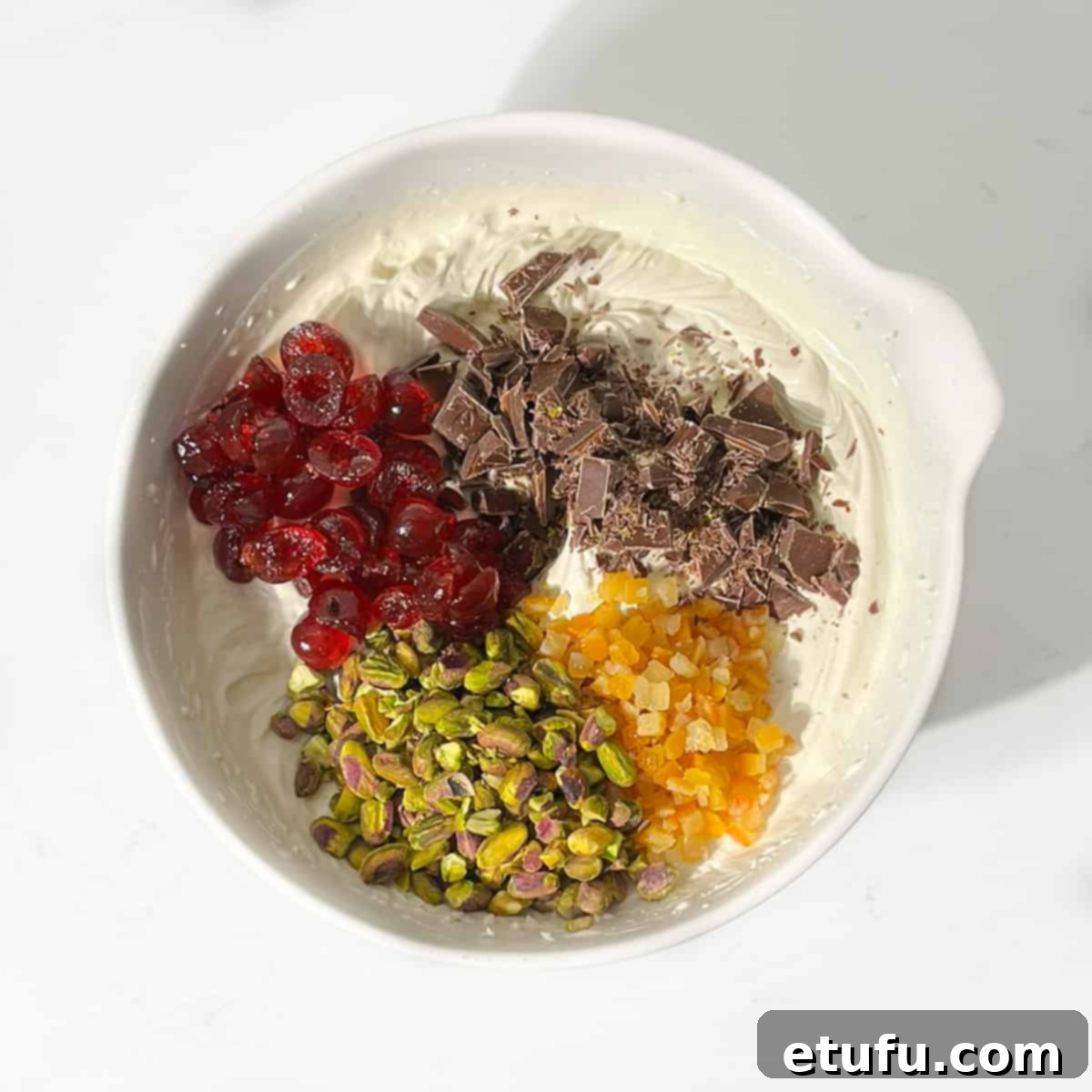 The vibrant medley of dried fruits, nuts, and chocolate being gently folded into the luscious, whipped Cassata ice cream mixture in a large bowl.