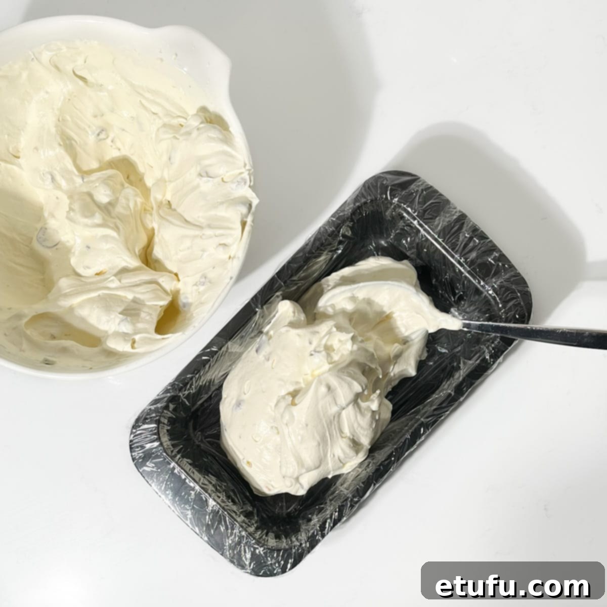 Scooping the rich, colorful Cassata ice cream mixture into the cling-film-lined loaf tin, filling it evenly.