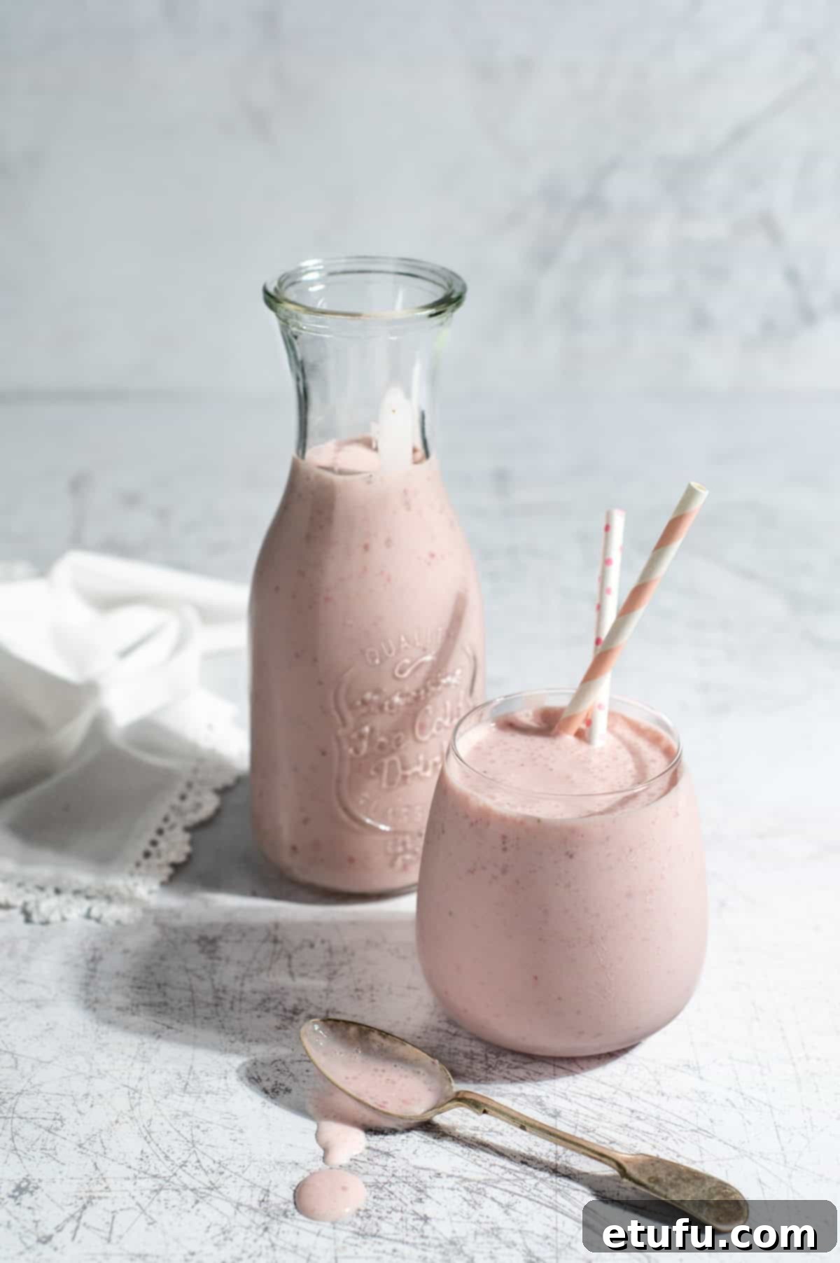 Creamy Strawberry Lassi 2 A glass and a carafe of strawberry lassi on a white background.