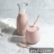 Creamy Strawberry Lassi 6 A glass and a carafe of strawberry lassi on a white background.