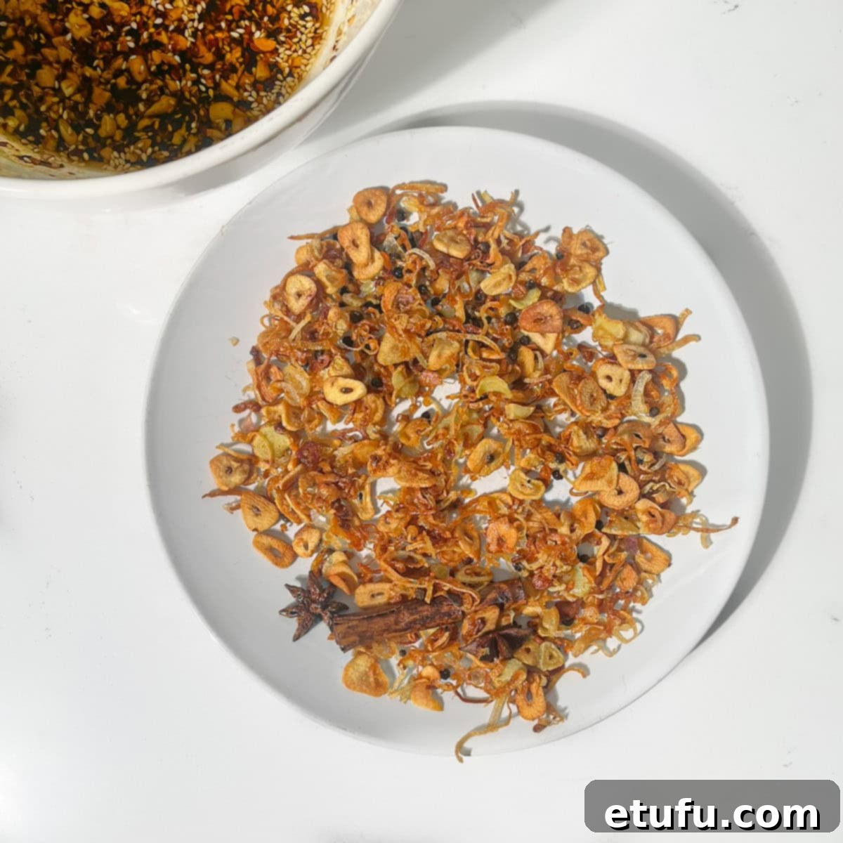 Fried shallots and garlic, golden and fragrant, are spread out on a plate lined with kitchen paper, cooling to achieve optimal crispiness.