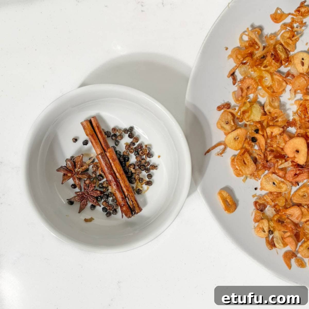 A hand gently sifts through the cooled chilli crisp mixture, picking out the larger whole spices like cinnamon sticks, star anise, and peppercorns before final combining.