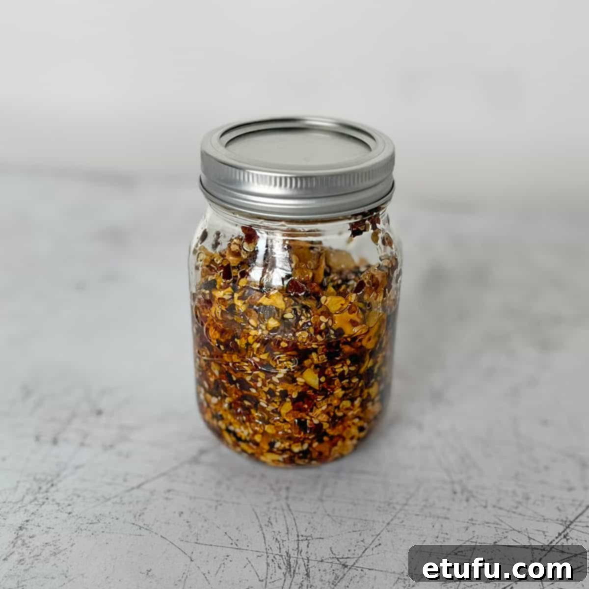 A jar of homemade chilli crisp oil, rich in color and texture, stands ready for use.