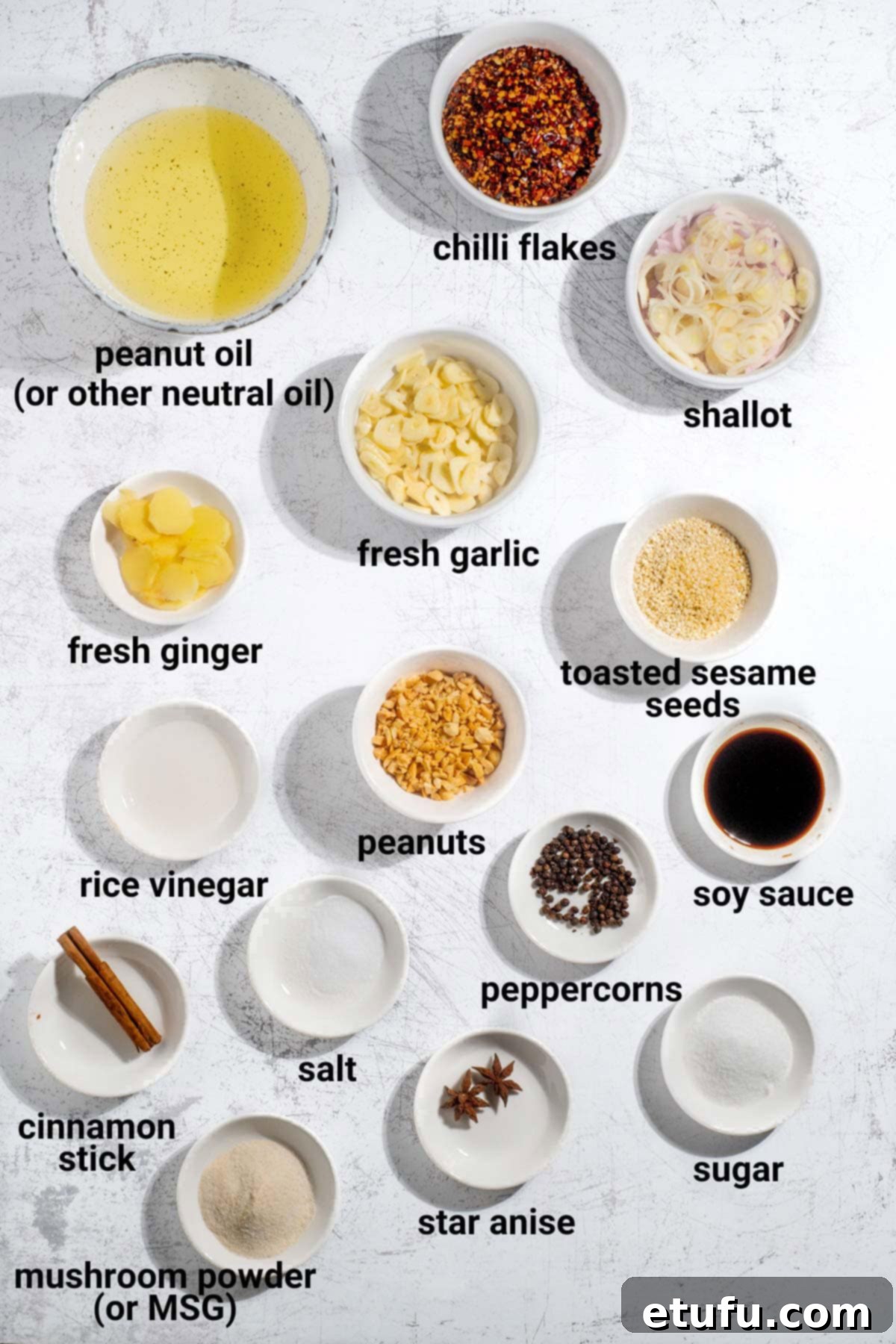 Various ingredients for crispy chilli oil, including fresh garlic, ginger, shallots, and different spices, laid out on a clean surface.