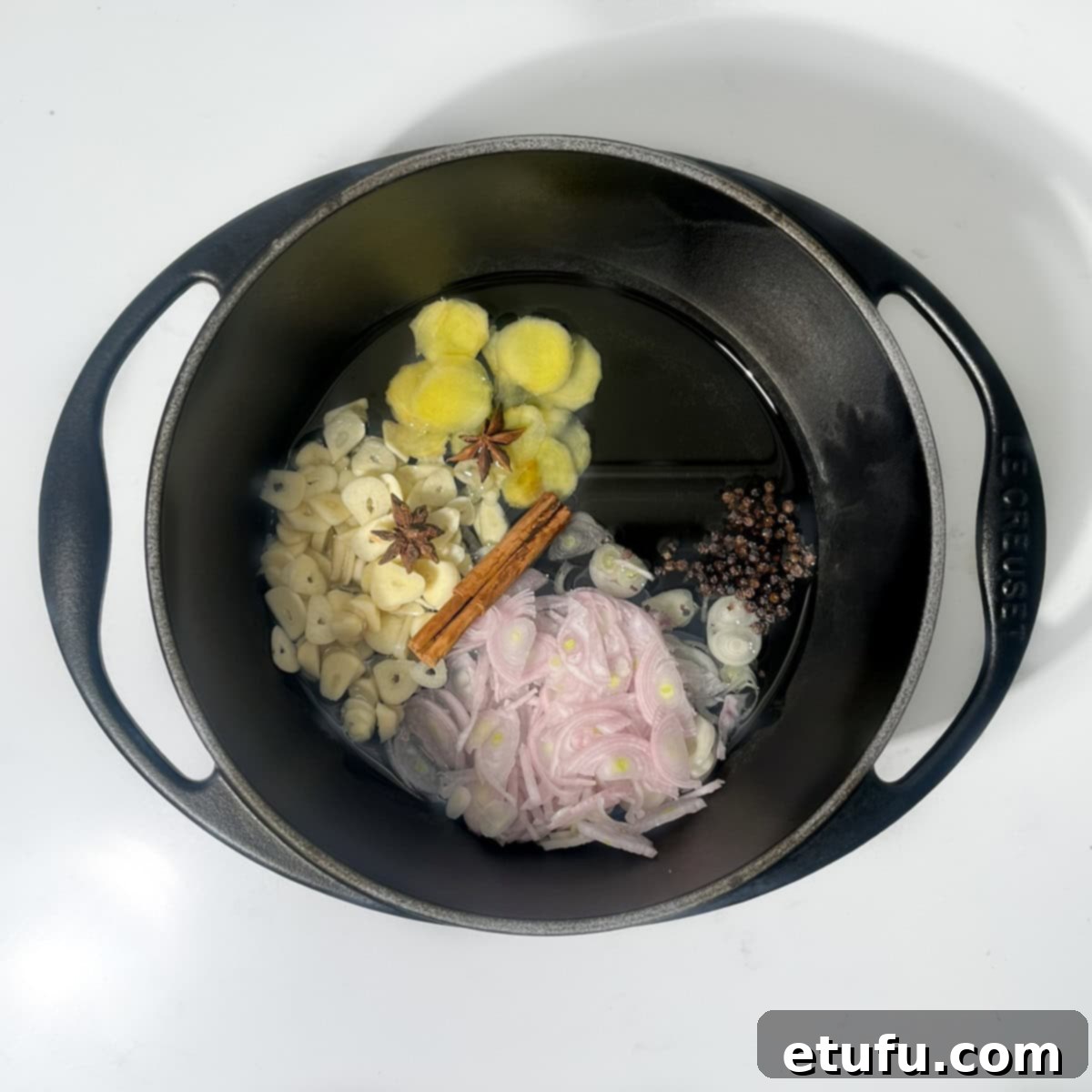 Peanut oil, thinly sliced shallots, garlic, ginger, a cinnamon stick, two star anise, and black peppercorns are gently simmering in a black saucepan over low heat.