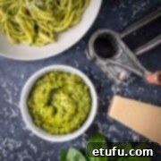 A bowl of pistachio pesto surrounded by a bowl of pasta, a parmesan grater and parmesan cheese.