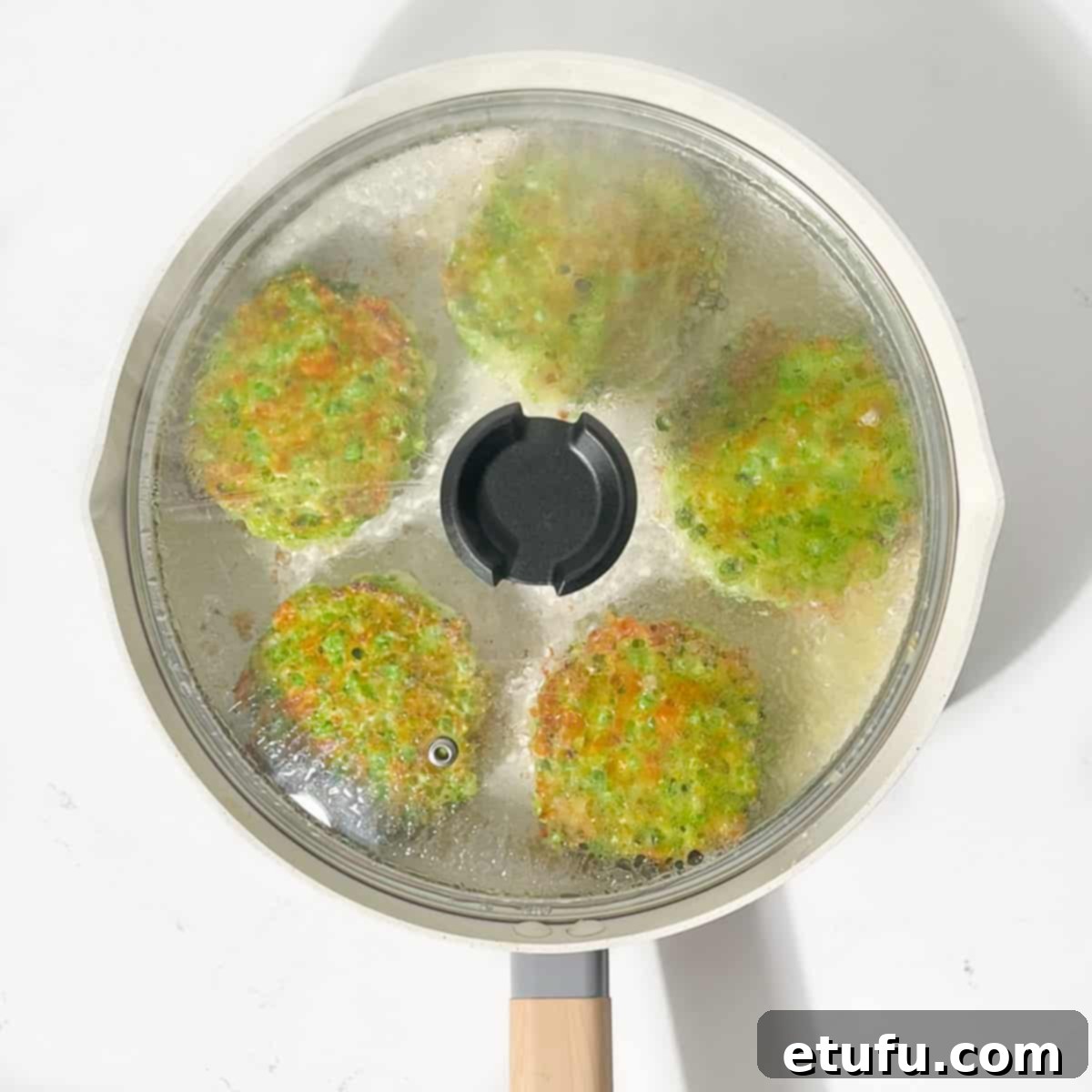 Green pea fritters frying in a large pan with the lid on, indicating even cooking and moisture retention.