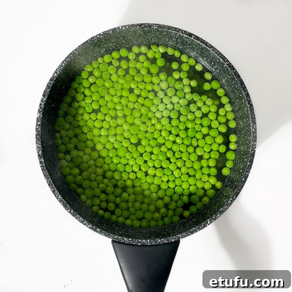 A small saucepan filled with boiling water and frozen petit pois, illustrating the first step of cooking the peas.