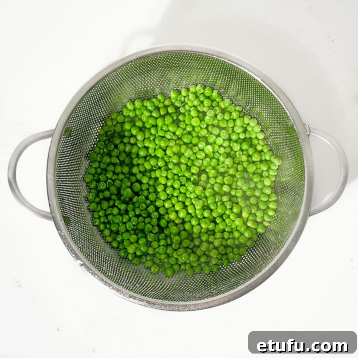 Cooked peas being drained in a colander under running cold water to halt the cooking process.